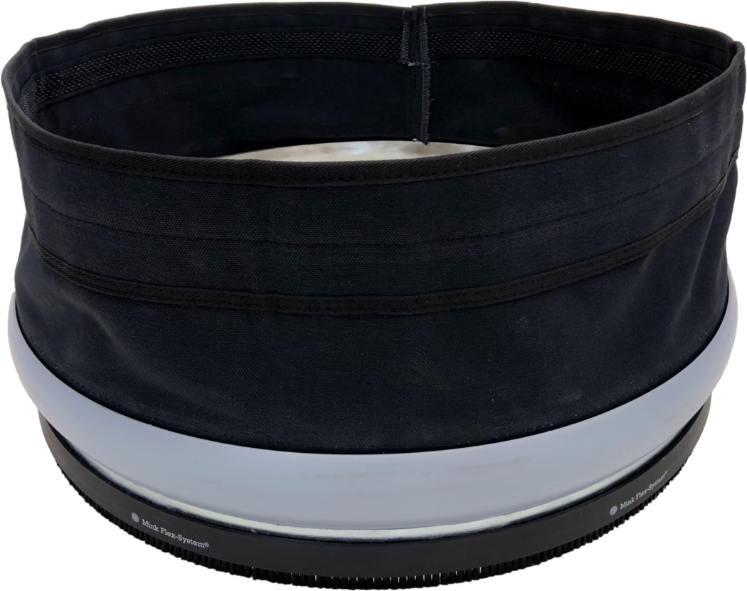 PALLMANN_dummy_SPIDER DUST SEALING SLEEVE_msl_2018-04 Close-up view of the top rim and opening of a cylindrical black fabric container or hat. The image shows a circular inner opening with black lining, visible reinforced stitching and several horizontal fabric bands on the exterior. Near the lower edge there are two wide light-gray plastic rings and a black ribbed rubber base with small teeth and partially visible printed text 'Mink Flex-System®'. The fabric has a coarse weave and a matte finish; the object appears structured yet flexible. Lighting is even and the background is white.